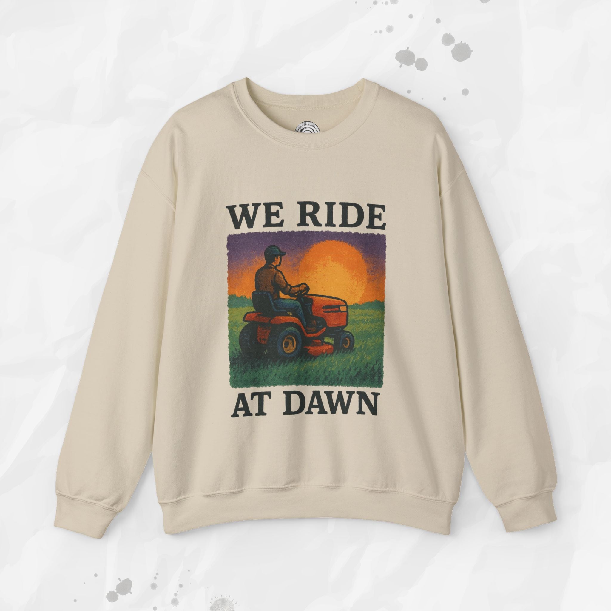 Beige sweatshirt with graphic of person on a tractor at sunset and text 'WE RIDE AT DAWN' on a white background.