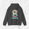 Dary grey hoodie with a colorful graphic and 'Stay Strange' text on the back against a light gray background.